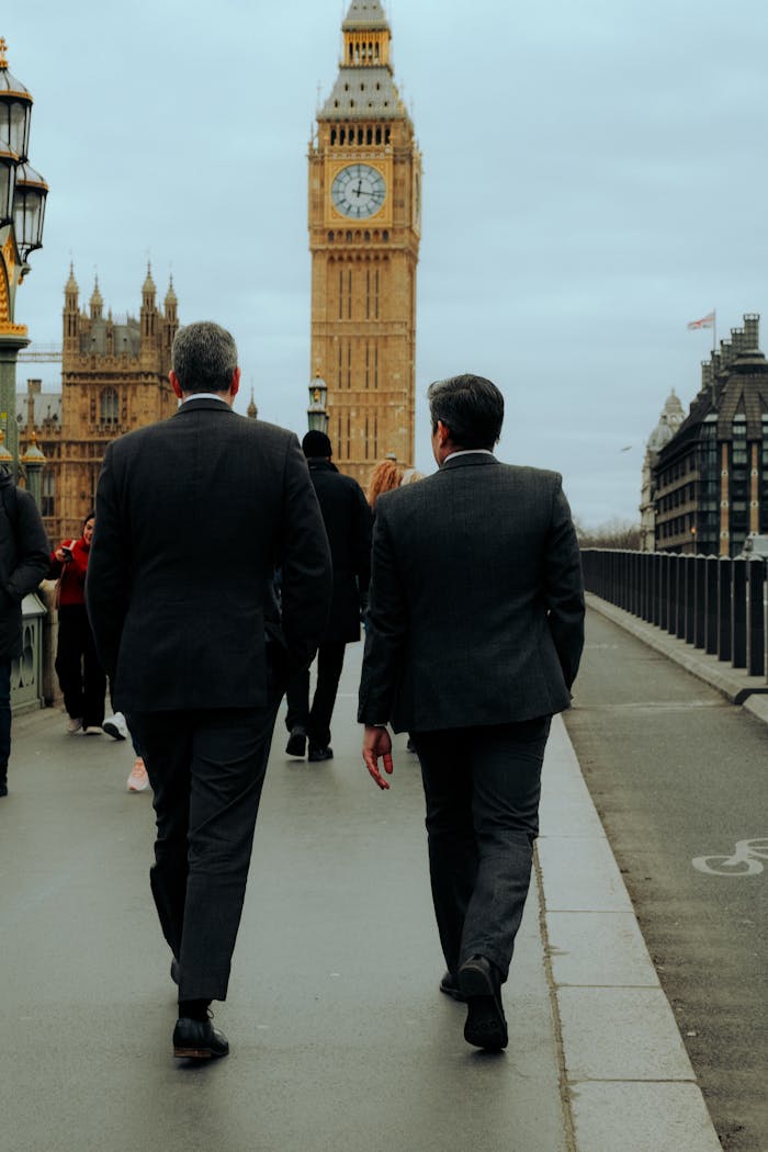 Two businessmen in suits walking along city streets with Big Ben in the background, London.