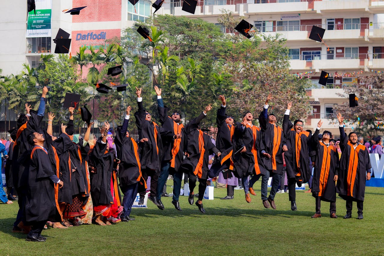 Graduates joyfully toss caps in the air during outdoor ceremony, celebrating graduation day.